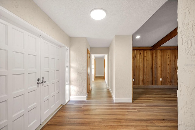 hallway with hardwood / wood-style floors, wooden walls, a textured ceiling, and beamed ceiling