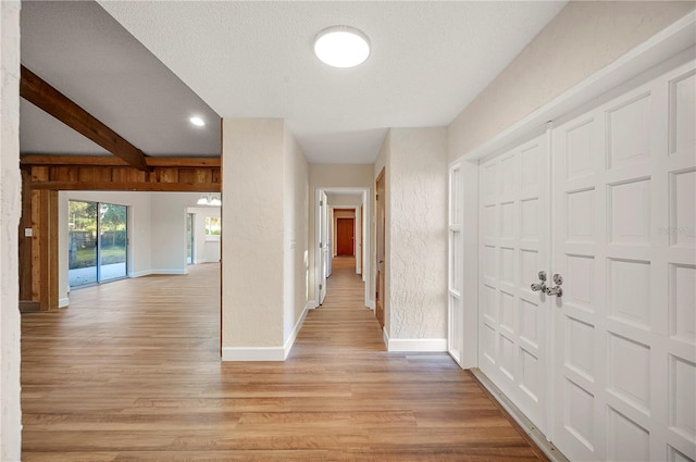 hall with beam ceiling, light wood-type flooring, and a textured ceiling