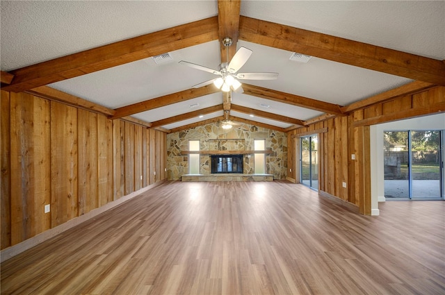 unfurnished living room with lofted ceiling, a stone fireplace, ceiling fan, a textured ceiling, and light hardwood / wood-style floors