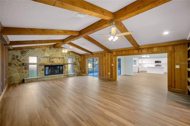 unfurnished living room with a stone fireplace, ceiling fan, a textured ceiling, and vaulted ceiling with beams