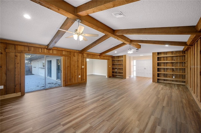 unfurnished living room featuring vaulted ceiling with beams, built in shelves, ceiling fan, and a textured ceiling