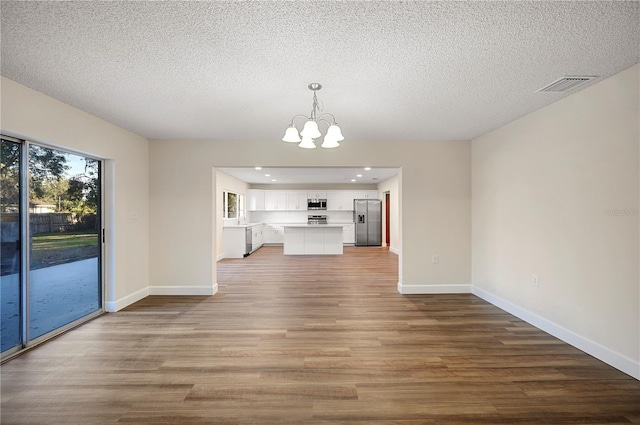 unfurnished living room with hardwood / wood-style flooring, a textured ceiling, and a chandelier