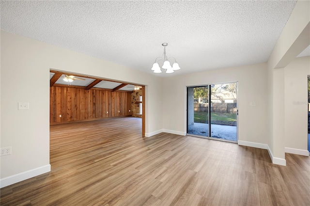 interior space with ceiling fan with notable chandelier, light wood-type flooring, a textured ceiling, and wooden walls