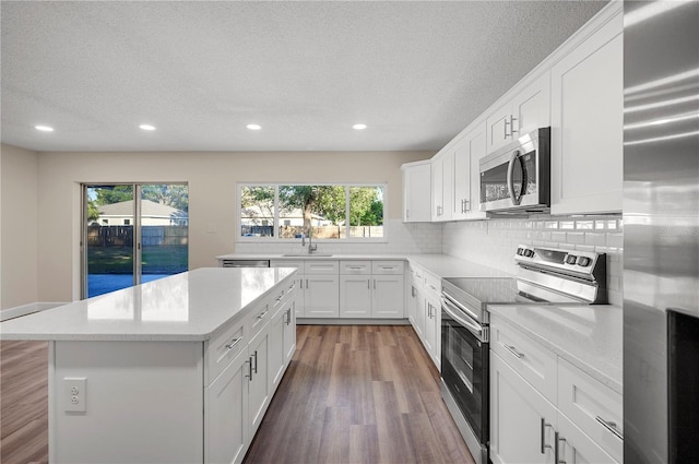 kitchen with a center island, backsplash, white cabinets, a textured ceiling, and stainless steel appliances