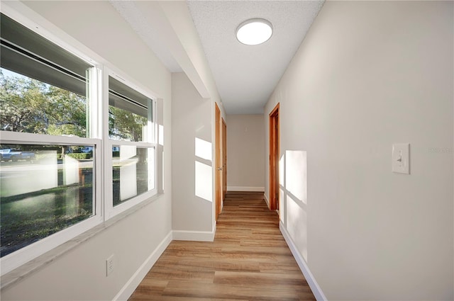 corridor featuring light wood-type flooring and a textured ceiling