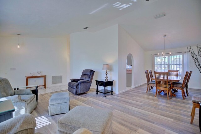 living room featuring a notable chandelier, light hardwood / wood-style flooring, and vaulted ceiling