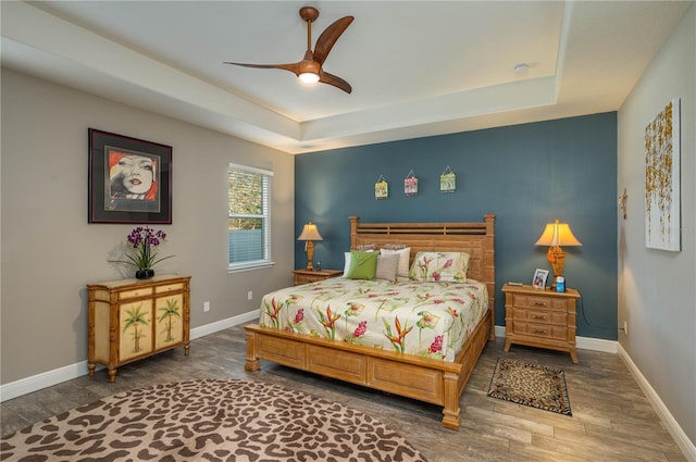 bedroom with a tray ceiling, dark wood-type flooring, and ceiling fan