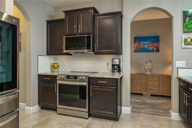 kitchen featuring tasteful backsplash, light stone countertops, appliances with stainless steel finishes, and dark brown cabinetry