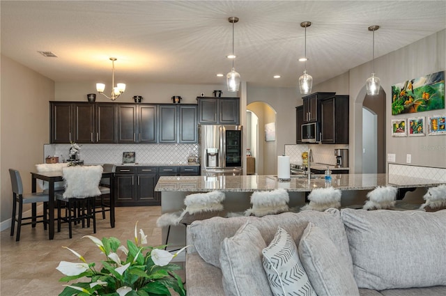 kitchen featuring a breakfast bar, hanging light fixtures, stainless steel appliances, light stone countertops, and decorative backsplash