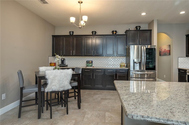 kitchen featuring light stone counters, a chandelier, stainless steel fridge with ice dispenser, pendant lighting, and backsplash