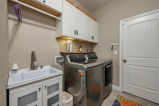 clothes washing area featuring washer and dryer, sink, cabinets, light tile patterned floors, and a textured ceiling