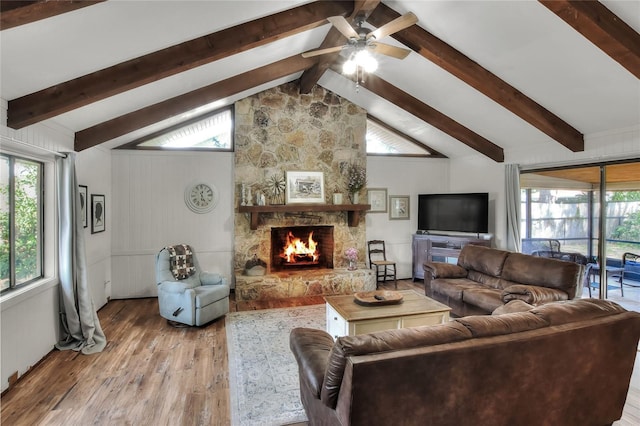 living room featuring ceiling fan, light hardwood / wood-style flooring, lofted ceiling with beams, and a stone fireplace