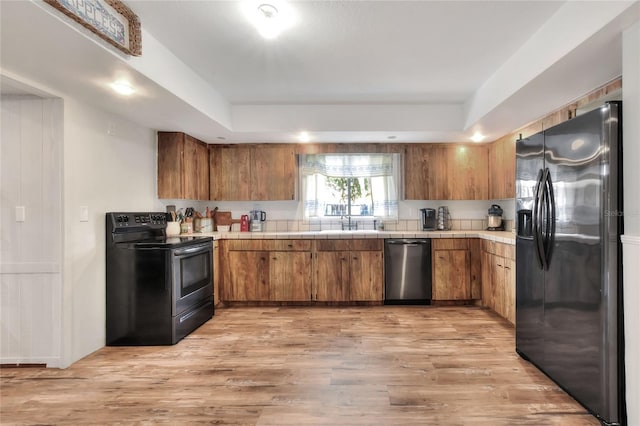 kitchen with appliances with stainless steel finishes, tile counters, sink, a raised ceiling, and light wood-type flooring