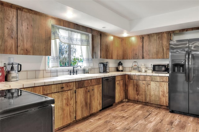 kitchen with light hardwood / wood-style floors, sink, black appliances, and tile counters