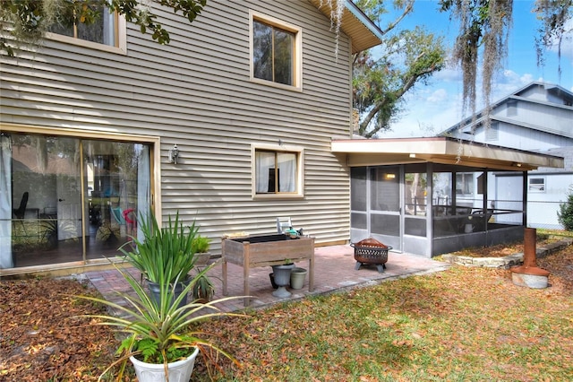 rear view of property featuring a sunroom, a patio area, and an outdoor fire pit