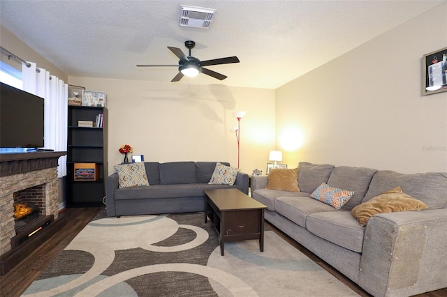 living room featuring a fireplace, a textured ceiling, dark hardwood / wood-style flooring, and ceiling fan