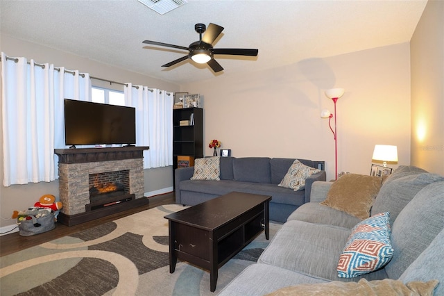 living room with a stone fireplace, ceiling fan, and wood-type flooring