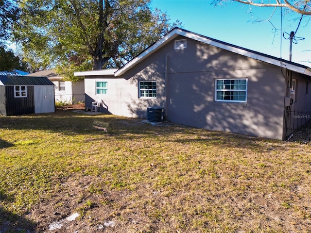 rear view of house featuring cooling unit, a storage shed, and a lawn