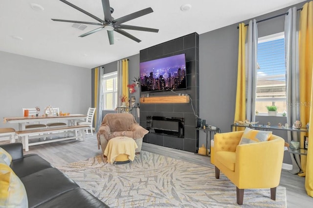 living room featuring ceiling fan, a tile fireplace, and light hardwood / wood-style flooring