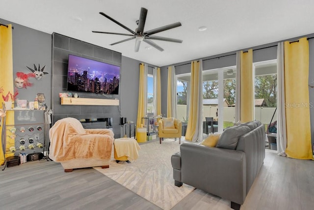 living room with ceiling fan, expansive windows, a tiled fireplace, and light hardwood / wood-style floors