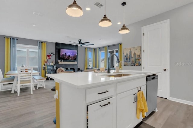 kitchen with white cabinetry, an island with sink, light wood-type flooring, hanging light fixtures, and sink