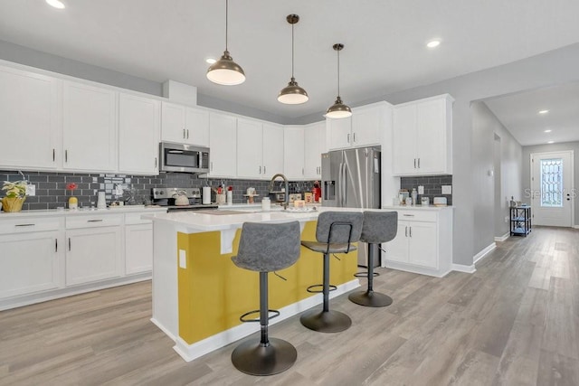 kitchen featuring decorative light fixtures, a kitchen bar, an island with sink, stainless steel appliances, and white cabinets