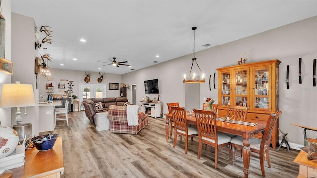 dining area with ceiling fan with notable chandelier, light wood-type flooring, and french doors