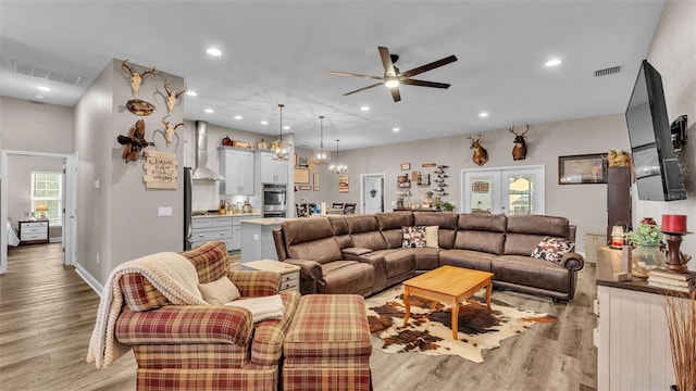 living room with french doors, ceiling fan with notable chandelier, and light hardwood / wood-style floors