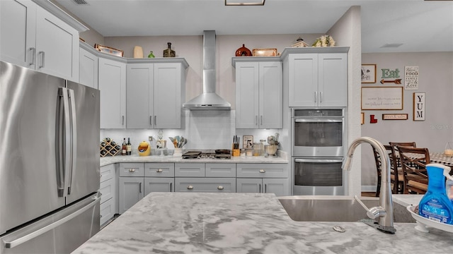 kitchen featuring decorative backsplash, appliances with stainless steel finishes, light stone counters, sink, and wall chimney range hood