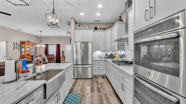 kitchen featuring decorative backsplash, light stone counters, stainless steel appliances, pendant lighting, and white cabinets