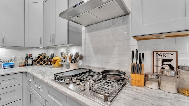 kitchen with light stone countertops, backsplash, stainless steel gas cooktop, and wall chimney range hood