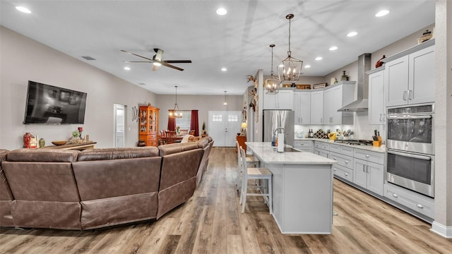 kitchen featuring a breakfast bar, a center island with sink, hanging light fixtures, and wall chimney range hood