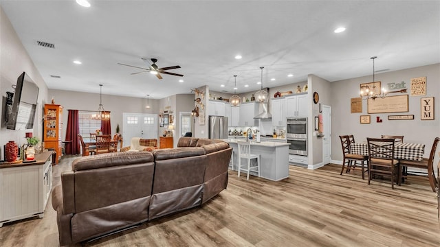 living room with ceiling fan with notable chandelier and light wood-type flooring