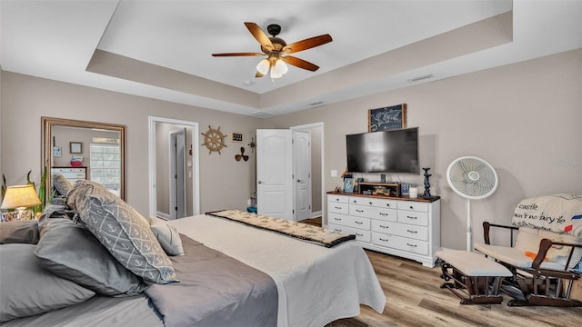 bedroom with wood-type flooring, a tray ceiling, and ceiling fan