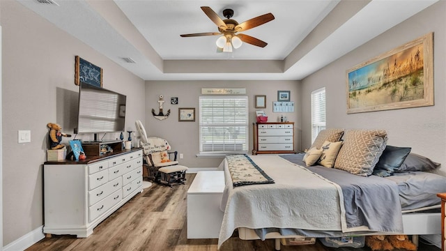 bedroom featuring ceiling fan, light hardwood / wood-style floors, and a tray ceiling