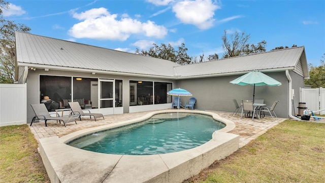 rear view of house featuring a sunroom, a fenced in pool, a patio, and a lawn