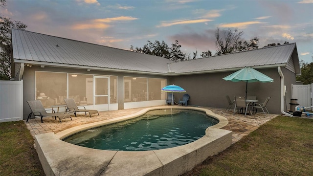 pool at dusk featuring a patio area and a sunroom