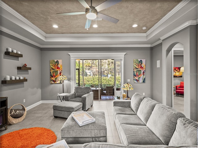 tiled living room with a raised ceiling, ceiling fan, and crown molding