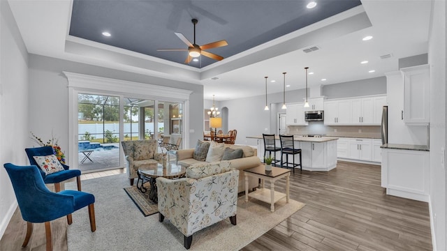 living room with ceiling fan with notable chandelier, a raised ceiling, light wood-type flooring, and ornamental molding