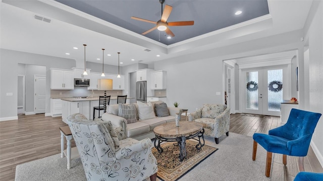 living room featuring ceiling fan, french doors, light wood-type flooring, and a tray ceiling