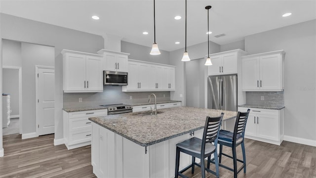 kitchen featuring pendant lighting, stainless steel appliances, an island with sink, white cabinets, and sink