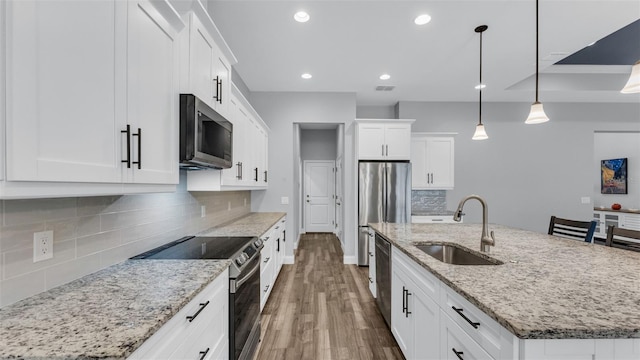 kitchen with a center island with sink, appliances with stainless steel finishes, pendant lighting, white cabinets, and sink