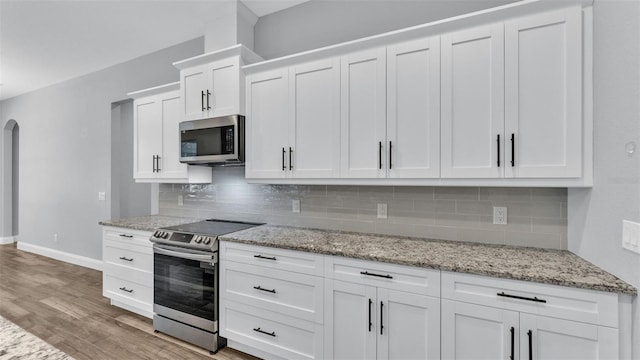 kitchen featuring light stone countertops, white cabinetry, light hardwood / wood-style flooring, and appliances with stainless steel finishes