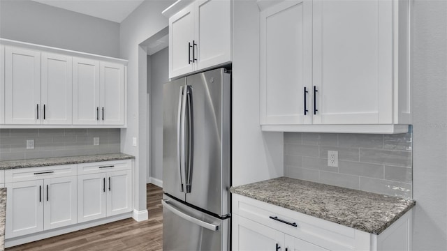 kitchen featuring wood-type flooring, stainless steel refrigerator, light stone countertops, decorative backsplash, and white cabinets