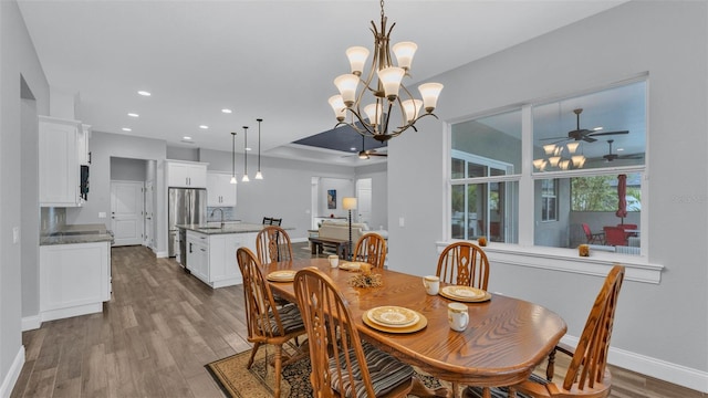 dining room with ceiling fan with notable chandelier, sink, and light wood-type flooring