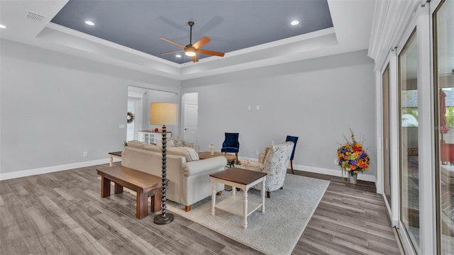 living room featuring ceiling fan, light wood-type flooring, crown molding, and a tray ceiling