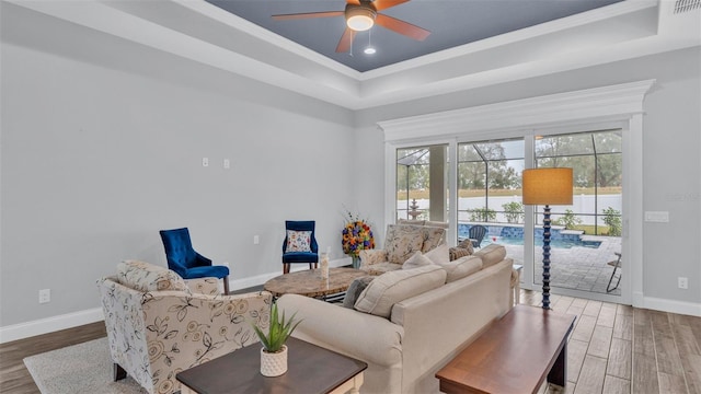 living room with ceiling fan, a tray ceiling, and hardwood / wood-style floors