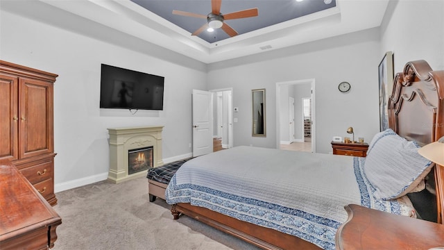 bedroom with ceiling fan, light colored carpet, and a tray ceiling