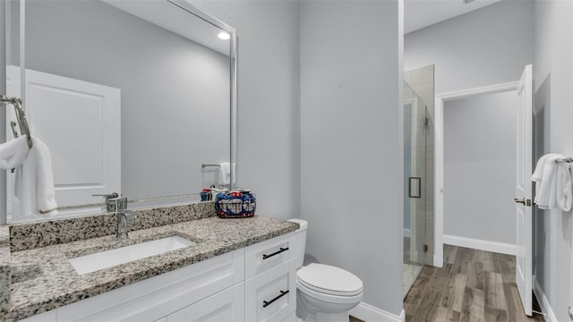 bathroom featuring wood-type flooring, toilet, vanity, and a shower with shower door