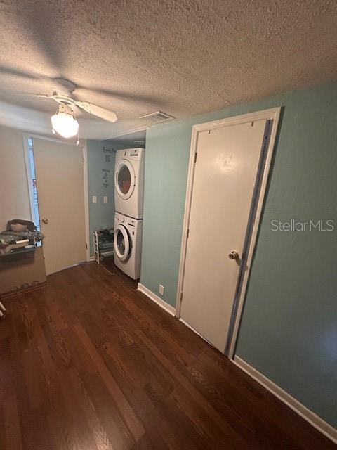 clothes washing area with ceiling fan, dark hardwood / wood-style floors, a textured ceiling, and stacked washer / dryer